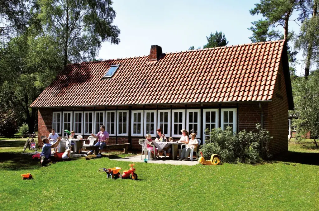 zwei Familien sitzt draußen in der Sonne vor einem Ferienhaus im DEW-Feriendorf Schneverdingen